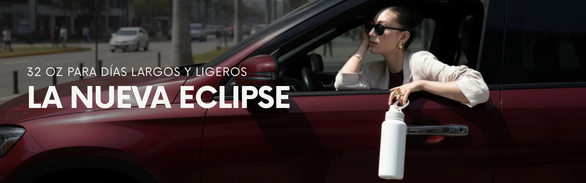 Mujer en auto sosteniendo una Eclipse Bottle blanca/cream de 32 oz por su asa ergonómica. Botella térmica de acero inoxidable de gran capacidad, ideal para días largos, tráfico en la ciudad y viajes por carretera.